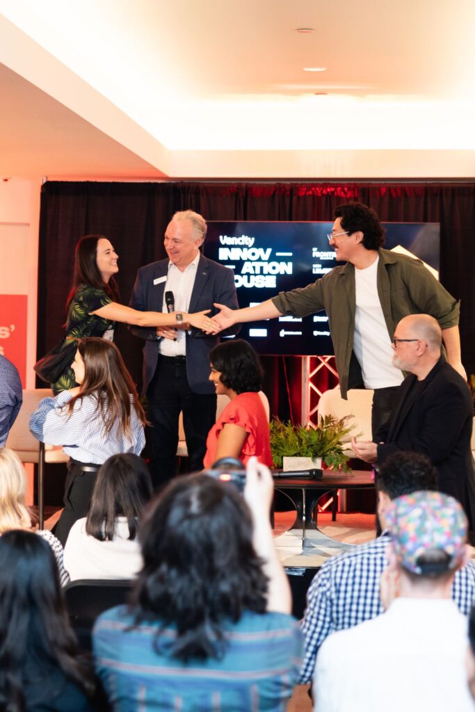 Ania Wysocka shaking hands on stage at Vancity Innovation House, with a moderator holding a microphone standing between her and another panelist, audience seated in the foreground