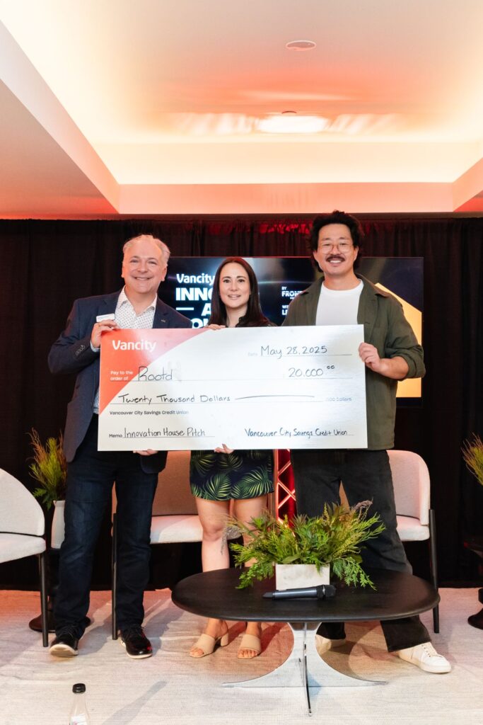 Ania Wysocka holding a $20,000 Vancity ceremonial check for Rootd at the Innovation House Pitch event, flanked by two representatives on stage, May 28 2025
