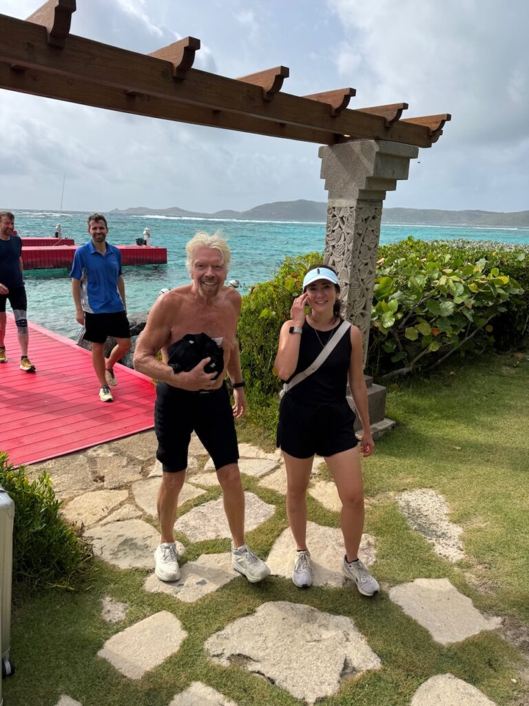 Ania Wysocka and Richard Branson standing on a stone path near a tropical waterfront dock, both in athletic wear after a workout